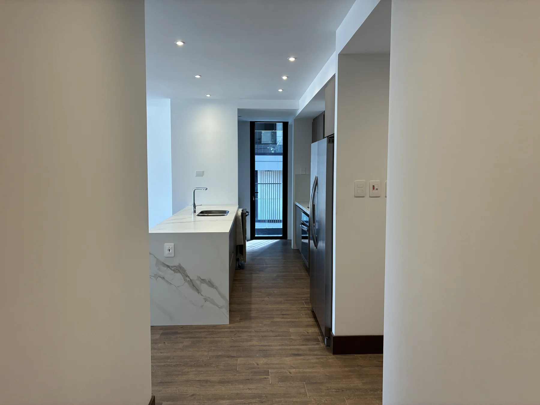 Vista desde la entrada hacia la cocina y la puerta del balcón en GAURA N-1601
